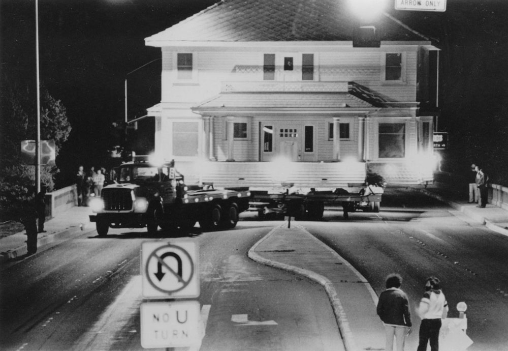 Black-and-white photograph of the house on a flatbed truck, being moved through San Luis Obispo at night